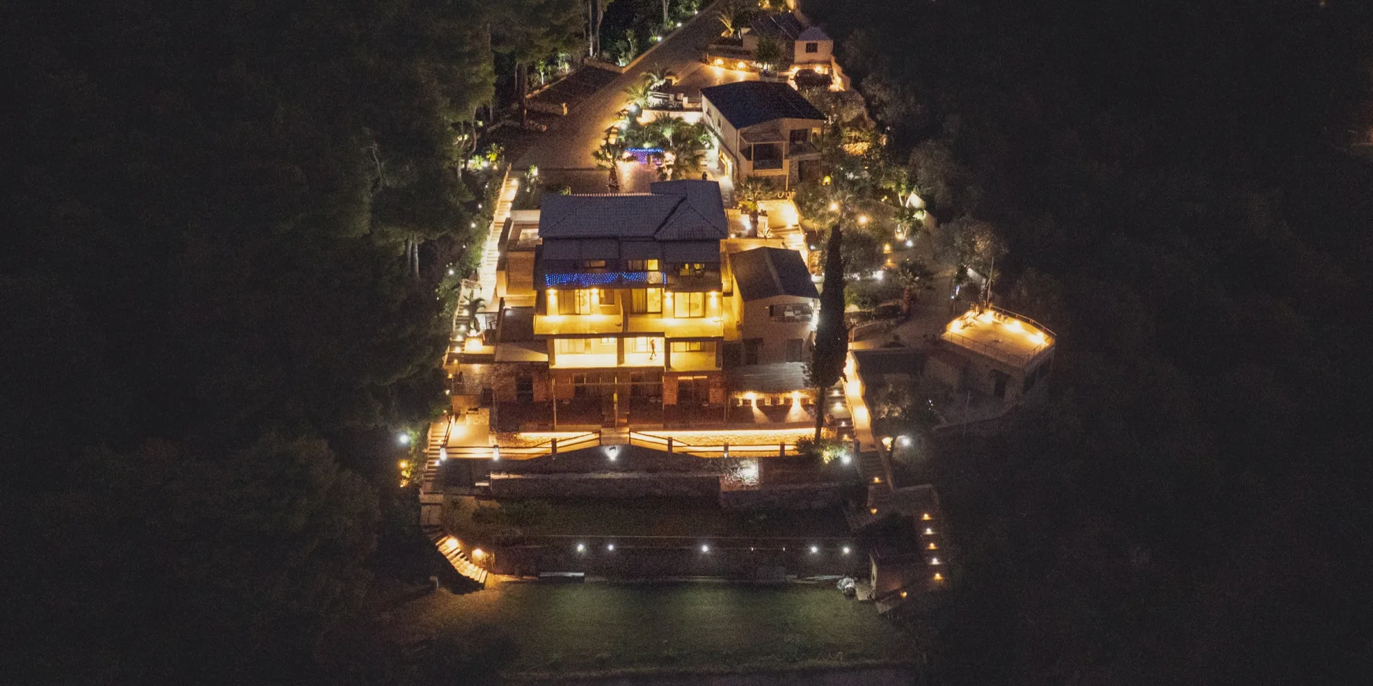 CORE Luxury Suites lit at night, seen from the air above the pines