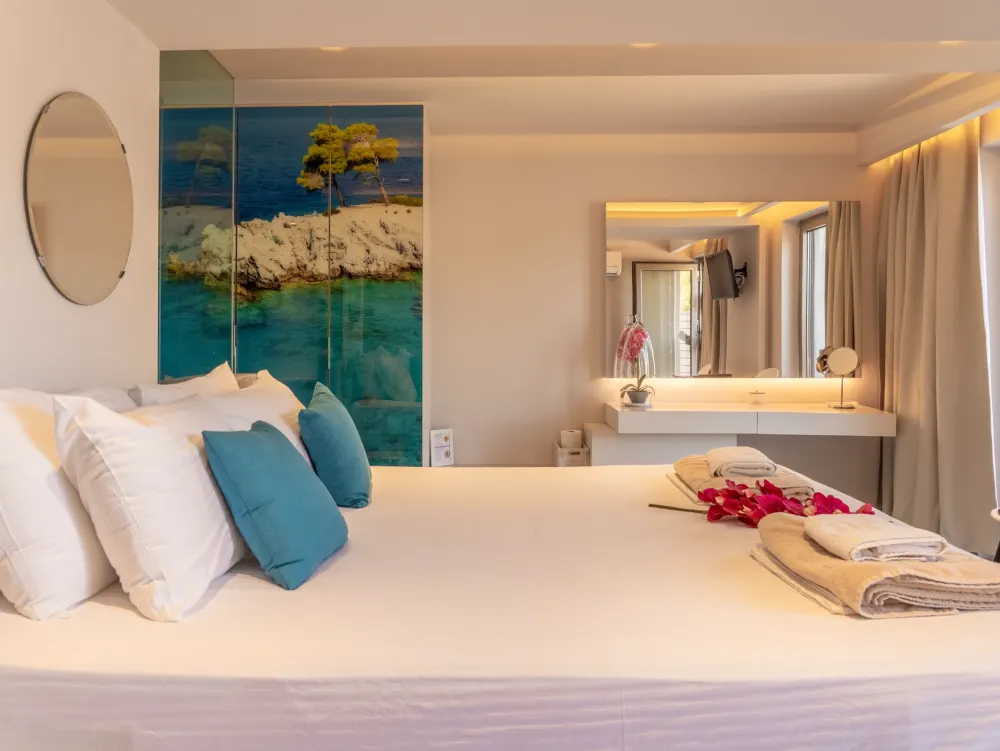 A suite bed beside a painted panel of pines above a bay