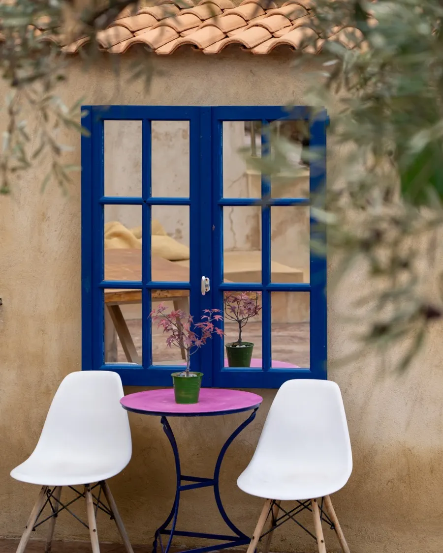 A blue-framed window and a small pink table in the courtyard